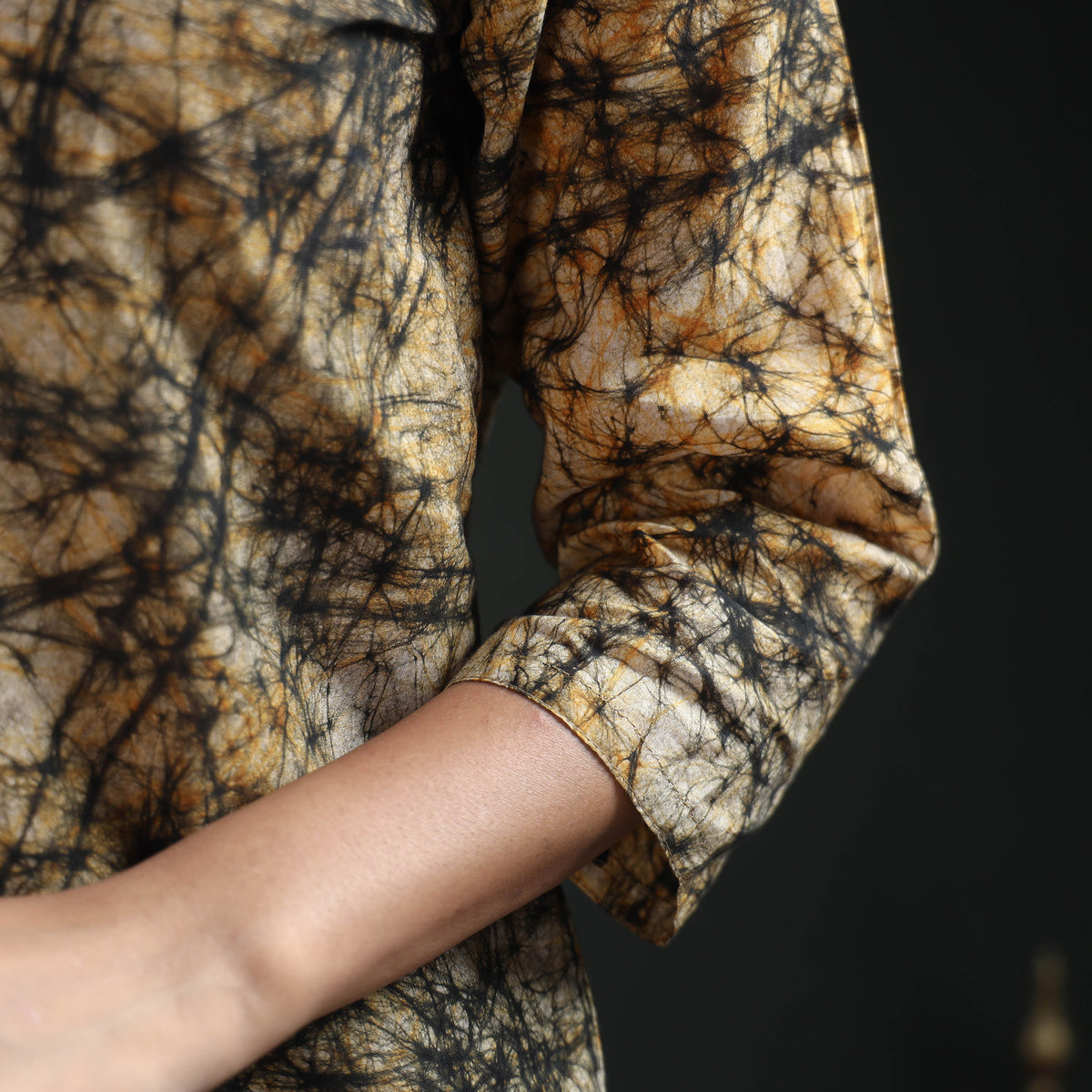 Close of the plain three-quarter sleeve on the beige kurta, the black web running to its edge
