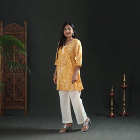 Three-quarter turn of the mustard yellow batik cotton kurta, full length, worn over cream pants
