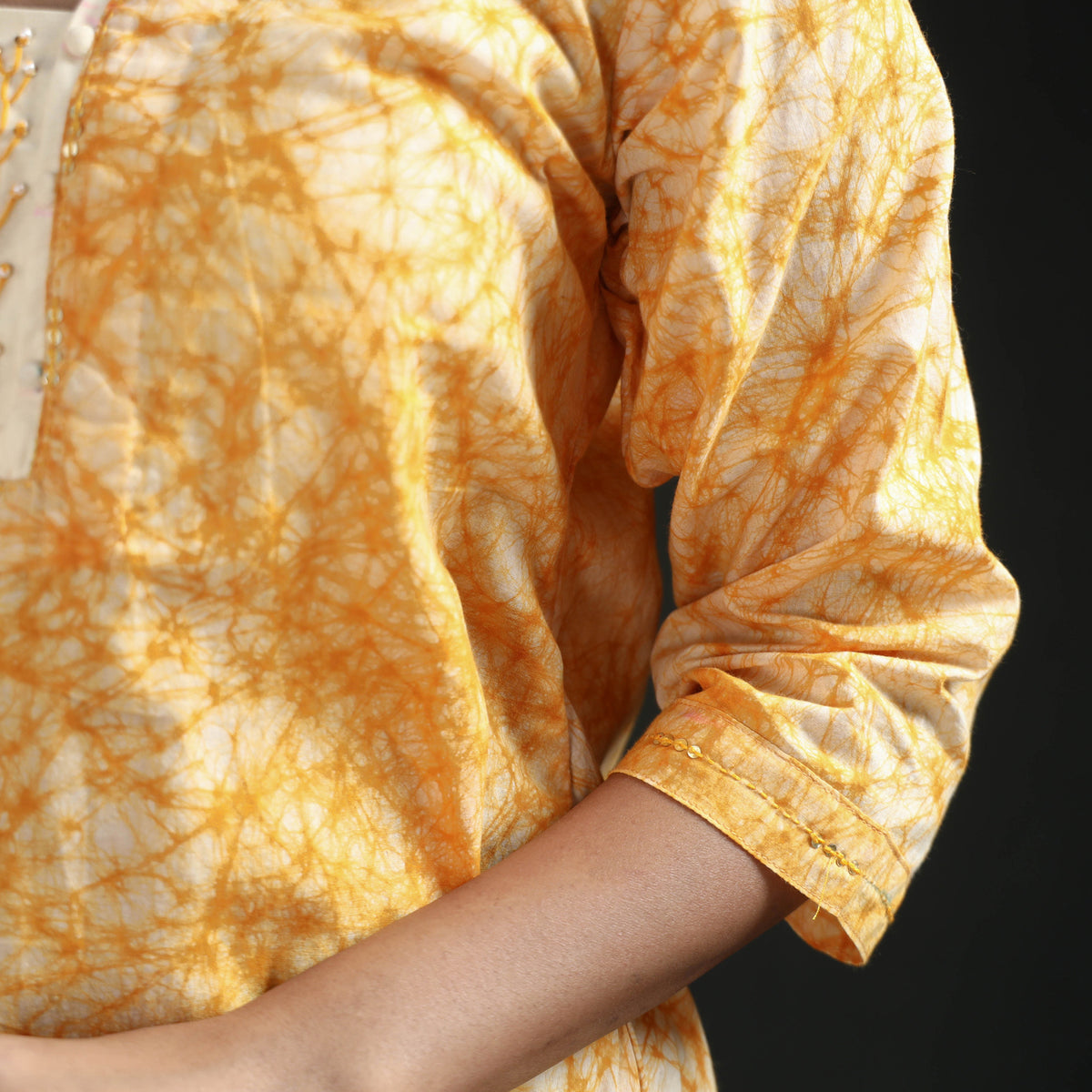 Cuff detail of the yellow kurta: cream piping and marbled batik veins