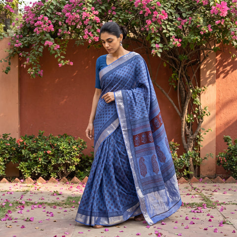 Blue Bagh Hand Block Print Natural Dyed Dola Silk Zari Border Saree, worn by a woman walking in a garden courtyard, AI visual of the saree, iTokri
