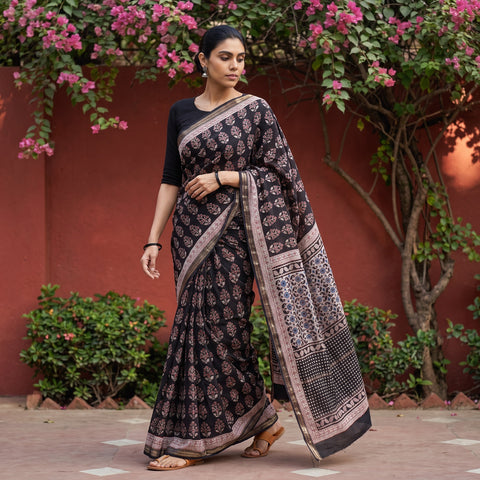 Black Bagh Hand Block Print Natural Dyed Maheshwari Silk Zari Border Saree, worn by a woman walking in a garden courtyard, AI visual of the saree, iTokri
