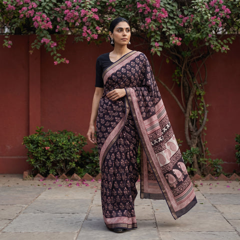 Black Bagh Hand Block Print Natural Dyed Maheshwari Silk Zari Border Saree, worn by a woman walking in a garden courtyard, AI visual of the saree, iTokri
