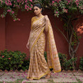 Yellow Bagh Hand Block Print Natural Dyed Maheshwari Silk Zari Border Saree, worn by a woman walking in a garden courtyard, AI visual of the saree, iTokri
