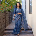 Blue Batik Hand Block Print Kota Doria Cotton Saree, worn by a woman on garden steps beside a white wall, AI visual of the saree, iTokri