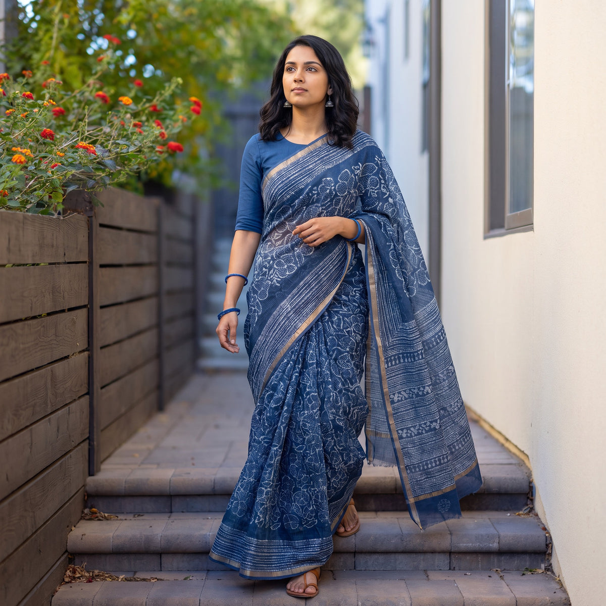 Blue Batik Hand Block Print Kota Doria Cotton Saree, worn by a woman on garden steps beside a white wall, AI visual of the saree, iTokri