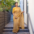 Mustard Batik Hand Block Print Kota Doria Cotton Saree, worn by a woman on garden steps beside a white wall, AI visual of the saree, iTokri