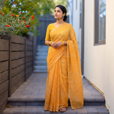Orange Batik Hand Block Print Kota Doria Cotton Saree, worn by a woman on garden steps beside a white wall, AI visual of the saree, iTokri
