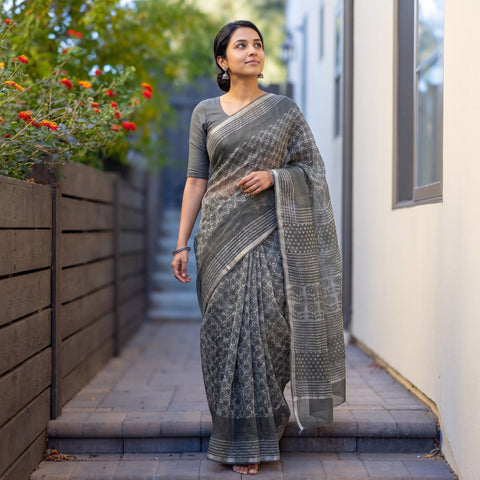 Grey Batik Hand Block Print Kota Doria Cotton Saree, worn by a woman on garden steps beside a white wall, AI visual of the saree, iTokri