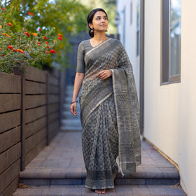 Grey Batik Hand Block Print Kota Doria Cotton Saree, worn by a woman on garden steps beside a white wall, AI visual of the saree, iTokri