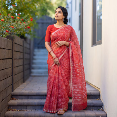 Red Batik Hand Block Print Kota Doria Cotton Saree, worn by a woman on garden steps beside a white wall, AI visual of the saree, iTokri