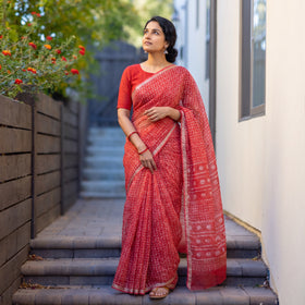 Red Batik Hand Block Print Kota Doria Cotton Saree, worn by a woman on garden steps beside a white wall, AI visual of the saree, iTokri