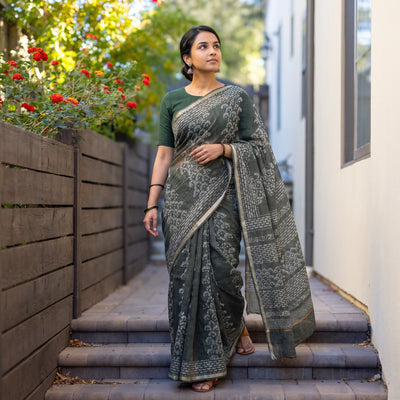 Grey Batik Hand Block Print Kota Doria Cotton Saree, worn by a woman on garden steps beside a white wall, AI visual of the saree, iTokri