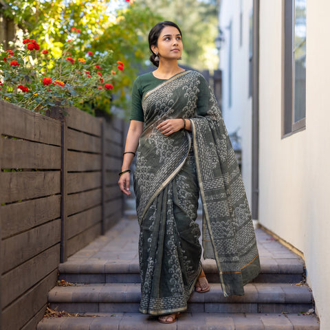 Grey Batik Hand Block Print Kota Doria Cotton Saree, worn by a woman on garden steps beside a white wall, AI visual of the saree, iTokri