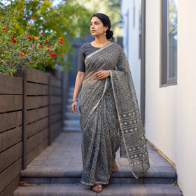 Grey Batik Hand Block Print Kota Doria Cotton Saree, worn by a woman on garden steps beside a white wall, AI visual of the saree, iTokri
