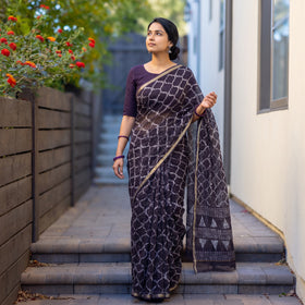 Black Batik Hand Block Print Kota Doria Cotton Saree, worn by a woman on garden steps beside a white wall, AI visual of the saree, iTokri