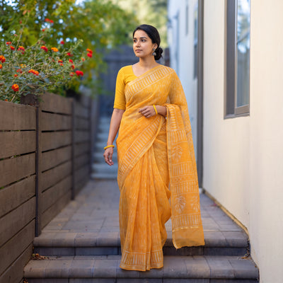 Orange Batik Hand Block Print Kota Doria Cotton Saree, worn by a woman on garden steps beside a white wall, AI visual of the saree, iTokri