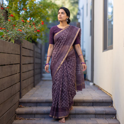 Purple Batik Hand Block Print Kota Doria Cotton Saree, worn by a woman on garden steps beside a white wall, AI visual of the saree, iTokri