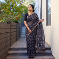Black Batik Hand Block Print Kota Doria Cotton Saree, worn by a woman on garden steps beside a white wall, AI visual of the saree, iTokri