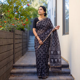 Black Batik Hand Block Print Kota Doria Cotton Saree, worn by a woman on garden steps beside a white wall, AI visual of the saree, iTokri