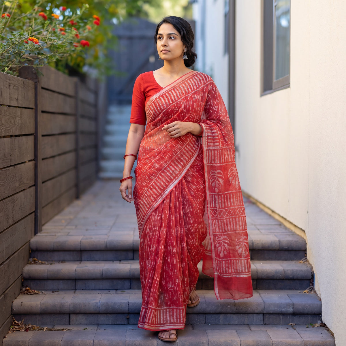 Red Batik Hand Block Print Kota Doria Cotton Saree, worn by a woman on garden steps beside a white wall, AI visual of the saree, iTokri