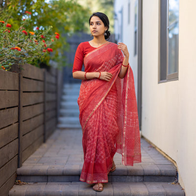 Red Batik Hand Block Print Kota Doria Cotton Saree, worn by a woman on garden steps beside a white wall, AI visual of the saree, iTokri