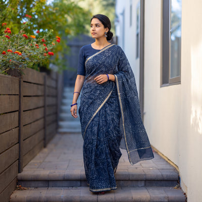 Blue Batik Hand Block Print Kota Doria Cotton Saree, worn by a woman on garden steps beside a white wall, AI visual of the saree, iTokri