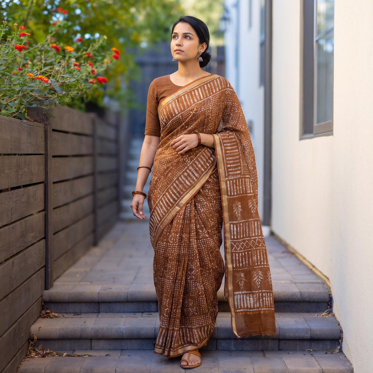 Brown Batik Hand Block Print Kota Doria Cotton Saree, worn by a woman on garden steps beside a white wall, AI visual of the saree, iTokri