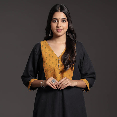 Front half-length view of a black wool kurta with a mustard printed yoke and cuffs, on a model