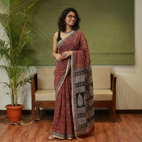 AI visual: model wearing the red natural dyed Kota Doria cotton saree with Bagh hand block print jaal and a black leaf motif pallu, in a living room