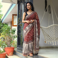 AI visual: model wearing the red natural dyed Kota Doria cotton saree with Bagh hand block print buti and a grey paisley pallu, on a sunlit verandah